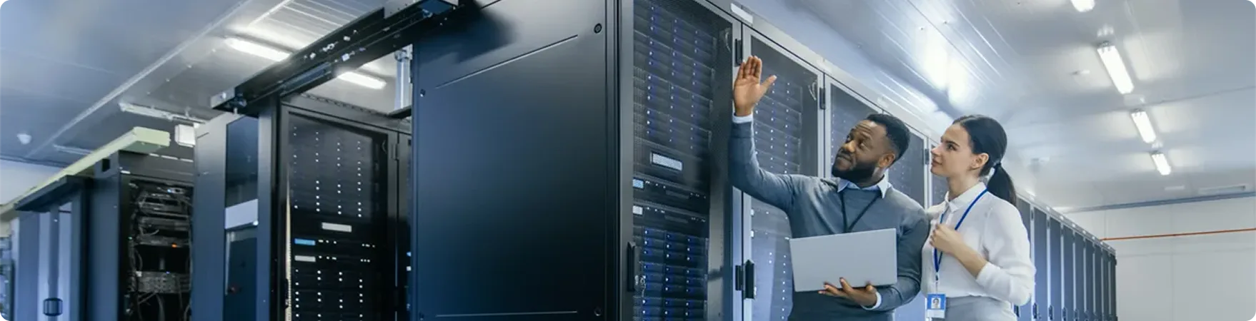 Black IT Technician with a Laptop Computer Gives a Tour to a Young Intern in the server room.