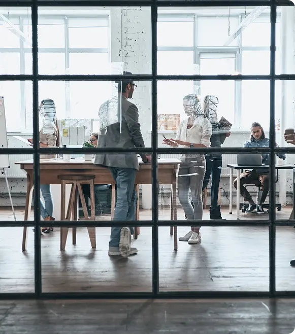 Large group of young modern people working and communicating together while standing behind the glass wall in the board room