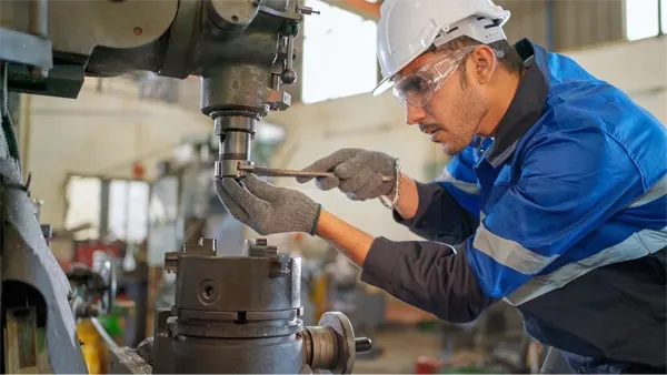 A man in a hard hat works on a piece of manufacturing equipment