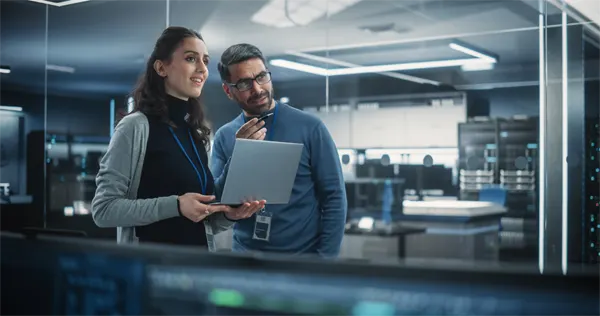 Portrait of Two Happy Female and Male Engineers Using Laptop Computer to Analyze and Discuss How to Proceed with the Artificial Intelligence Software. Casually Chatting in High Tech Research Office