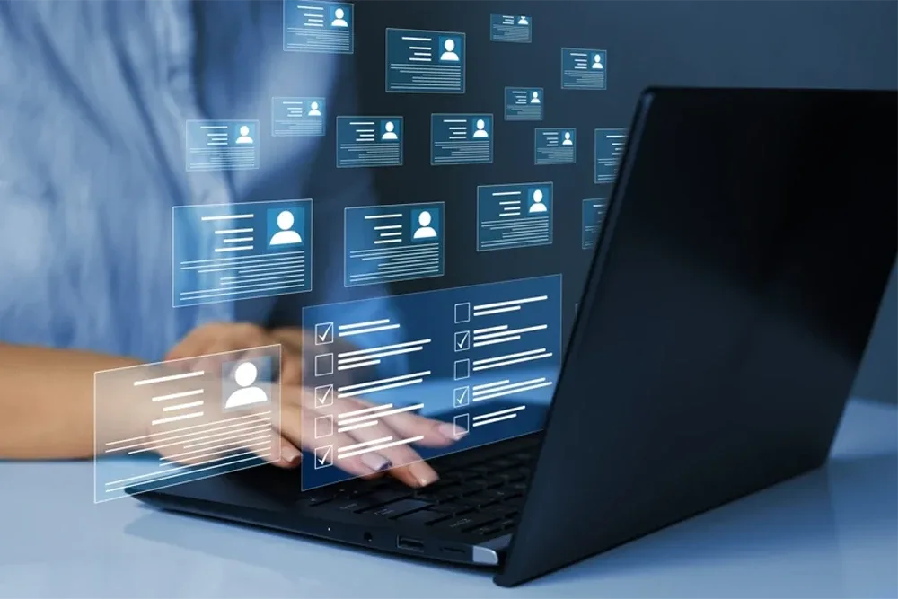 Person using a laptop with overlaid digital profile cards and checklists, representing employee or applicant management and evaluation.